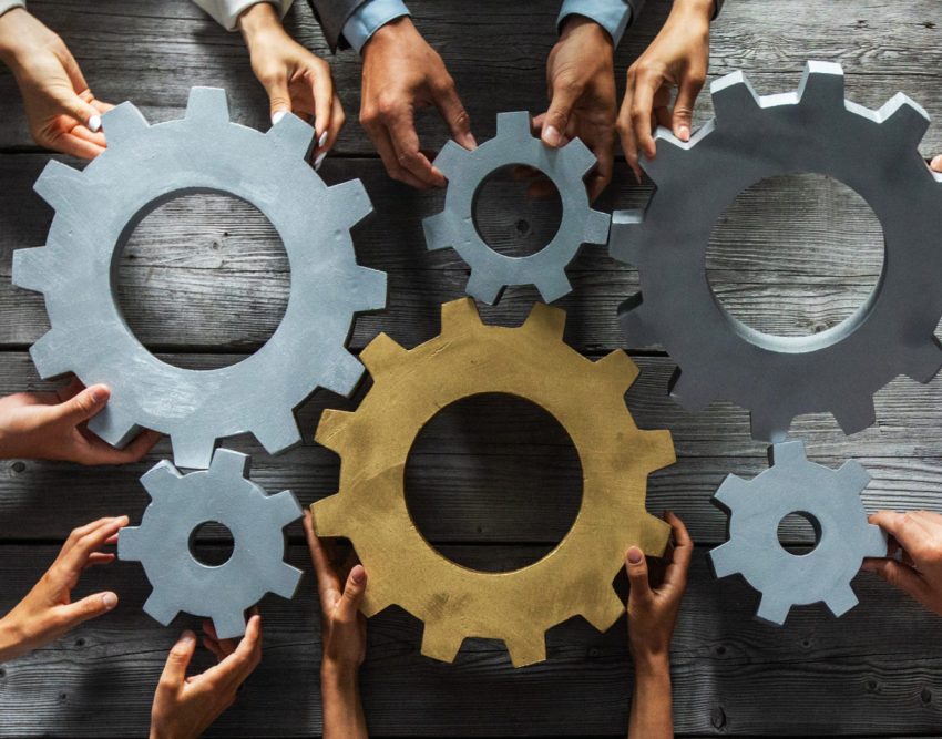 Group of business people joining together silver and golden colored gears on table at workplace top view